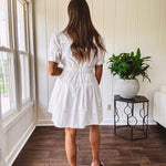 Fully lined white button down front dress with mock neck, V neck, short puffed sleeves, front pocket and elastic bands at the waist for a cinched waist look.