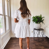 Fully lined white button down front dress with mock neck, V neck, short puffed sleeves, front pocket and elastic bands at the waist for a cinched waist look.