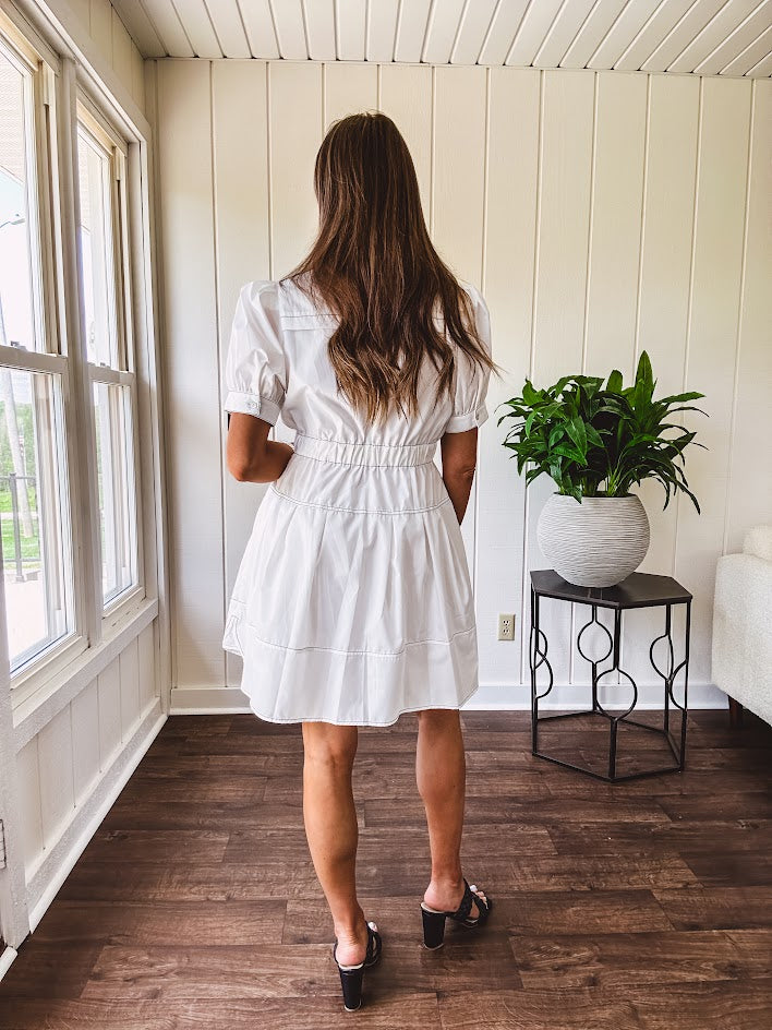 Fully lined white button down front dress with mock neck, V neck, short puffed sleeves, front pocket and elastic bands at the waist for a cinched waist look.