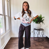 Black vinyl cargo pants with drawstring cuffs and cargo pockets topped with a denim waist band in a V shape with a button and zipper closure.