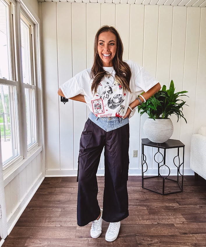 Black vinyl cargo pants with drawstring cuffs and cargo pockets topped with a denim waist band in a V shape with a button and zipper closure.