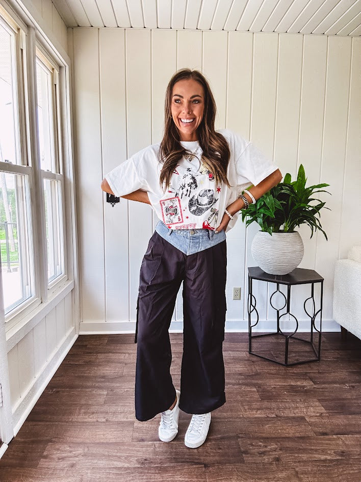 Black vinyl cargo pants with drawstring cuffs and cargo pockets topped with a denim waist band in a V shape with a button and zipper closure.