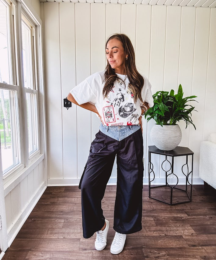 Black vinyl cargo pants with drawstring cuffs and cargo pockets topped with a denim waist band in a V shape with a button and zipper closure.