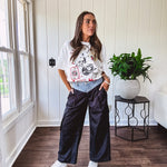 Black vinyl cargo pants with drawstring cuffs and cargo pockets topped with a denim waist band in a V shape with a button and zipper closure.