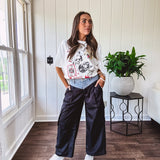 Black vinyl cargo pants with drawstring cuffs and cargo pockets topped with a denim waist band in a V shape with a button and zipper closure.