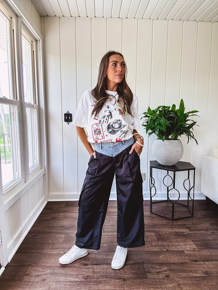 Black vinyl cargo pants with drawstring cuffs and cargo pockets topped with a denim waist band in a V shape with a button and zipper closure.