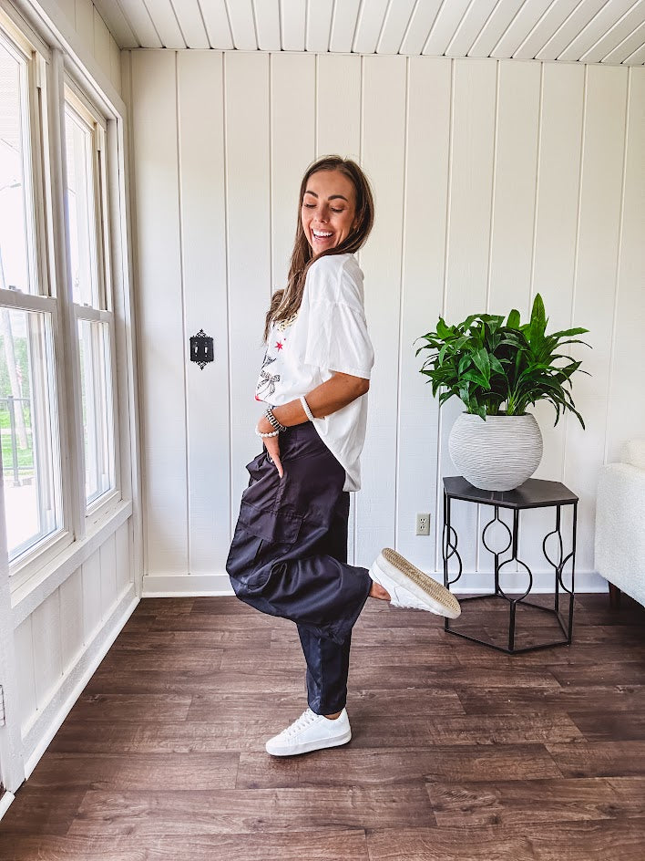 Black vinyl cargo pants with drawstring cuffs and cargo pockets topped with a denim waist band in a V shape with a button and zipper closure.