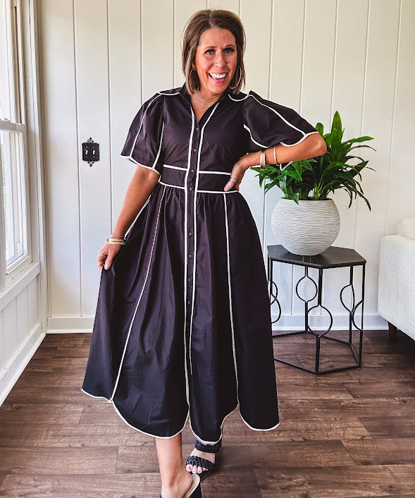 Black cotton maxi dress with white piping, collar, puff sleeve, scalloped hem, lined skirt and button down front.