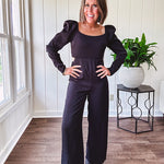 Black silky jumpsuit with puffed long sleeves, square neckline, side cutouts, elastic at the back waist and a tie at the back neckline.