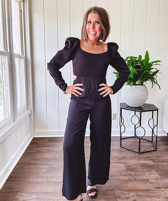 Black silky jumpsuit with puffed long sleeves, square neckline, side cutouts, elastic at the back waist and a tie at the back neckline.