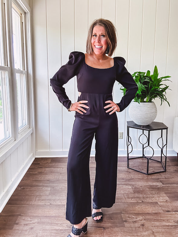 Black silky jumpsuit with puffed long sleeves, square neckline, side cutouts, elastic at the back waist and a tie at the back neckline.