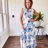 Lightweight cream sleeveless midi dress featuring blue and black large florals throughout, wooden buttons down to the lined tiered skirt, collar and matching belt.