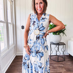 Lightweight cream sleeveless midi dress featuring blue and black large florals throughout, wooden buttons down to the lined tiered skirt, collar and matching belt.