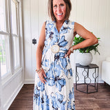 Lightweight cream sleeveless midi dress featuring blue and black large florals throughout, wooden buttons down to the lined tiered skirt, collar and matching belt.