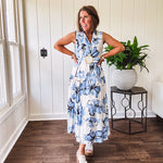Lightweight cream sleeveless midi dress featuring blue and black large florals throughout, wooden buttons down to the lined tiered skirt, collar and matching belt.