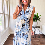 Lightweight cream sleeveless midi dress featuring blue and black large florals throughout, wooden buttons down to the lined tiered skirt, collar and matching belt.