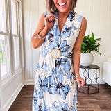 Lightweight cream sleeveless midi dress featuring blue and black large florals throughout, wooden buttons down to the lined tiered skirt, collar and matching belt.