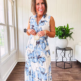 Lightweight cream sleeveless midi dress featuring blue and black large florals throughout, wooden buttons down to the lined tiered skirt, collar and matching belt.