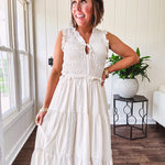 Oatmeal colored sleeveless midi dress with ruffled sleeves and collar with a tie, wide smocked bodice and lined, tiered skirt.