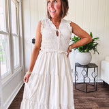 Oatmeal colored sleeveless midi dress with ruffled sleeves and collar with a tie, wide smocked bodice and lined, tiered skirt.