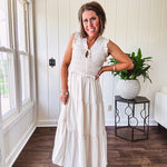 Oatmeal colored sleeveless midi dress with ruffled sleeves and collar with a tie, wide smocked bodice and lined, tiered skirt.