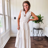 Oatmeal colored sleeveless midi dress with ruffled sleeves and collar with a tie, wide smocked bodice and lined, tiered skirt.