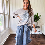 Light wash Tencel bloomer style pants with elastic, smocked waist band, front pockets with bow details and ruffled, angled hem.