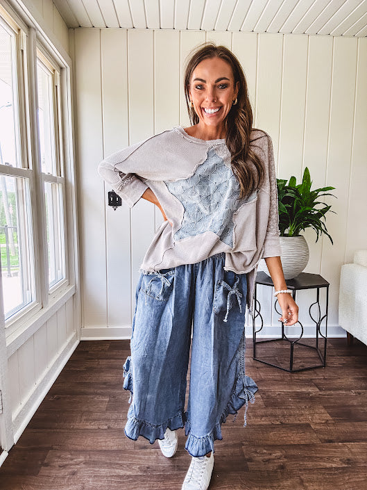 Light wash Tencel bloomer style pants with elastic, smocked waist band, front pockets with bow details and ruffled, angled hem.