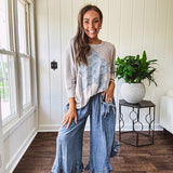 Light wash Tencel bloomer style pants with elastic, smocked waist band, front pockets with bow details and ruffled, angled hem.