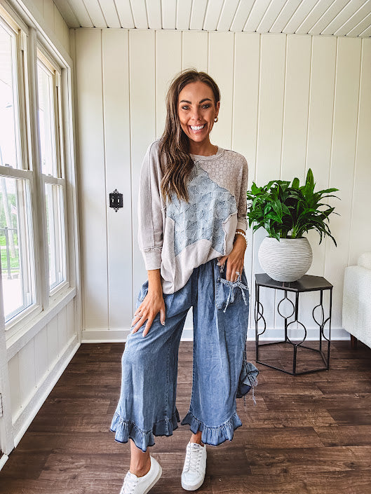 Light wash Tencel bloomer style pants with elastic, smocked waist band, front pockets with bow details and ruffled, angled hem.