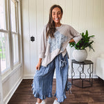 Light wash Tencel bloomer style pants with elastic, smocked waist band, front pockets with bow details and ruffled, angled hem.