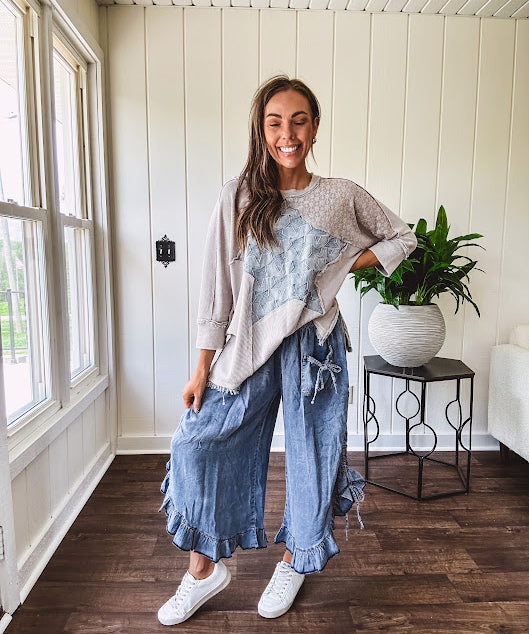 Light wash Tencel bloomer style pants with elastic, smocked waist band, front pockets with bow details and ruffled, angled hem.
