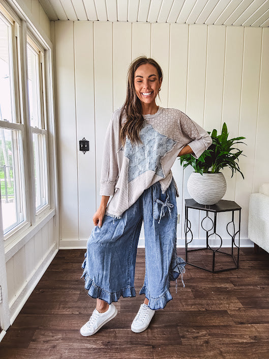 Light wash Tencel bloomer style pants with elastic, smocked waist band, front pockets with bow details and ruffled, angled hem.