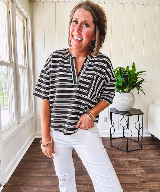 Black and white striped boxy cut Henley style knit top with 4 wooden buttons at the V neck, front pocket, short sleeves and shorter U shaped hem.