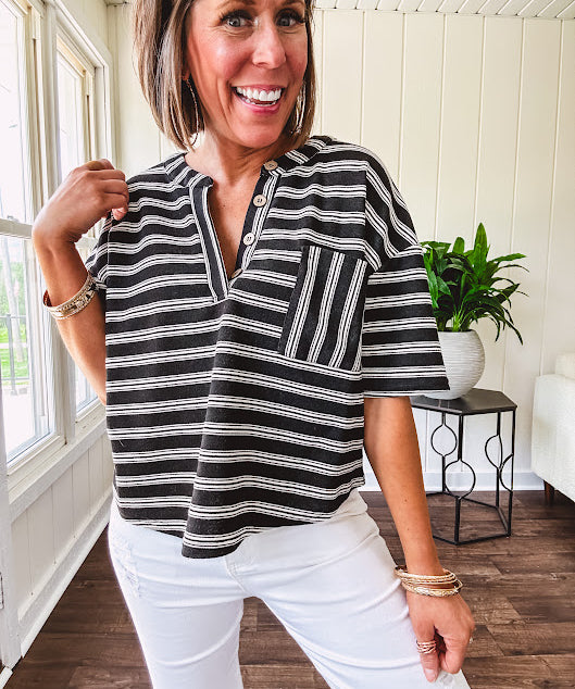 Black and white striped boxy cut Henley style knit top with 4 wooden buttons at the V neck, front pocket, short sleeves and shorter U shaped hem.