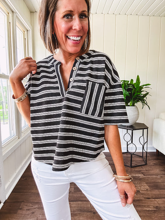 Black and white striped boxy cut Henley style knit top with 4 wooden buttons at the V neck, front pocket, short sleeves and shorter U shaped hem.