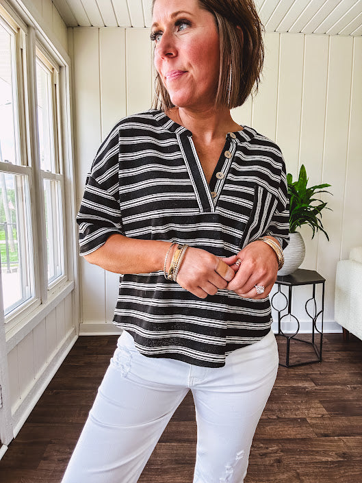 Black and white striped boxy cut Henley style knit top with 4 wooden buttons at the V neck, front pocket, short sleeves and shorter U shaped hem.