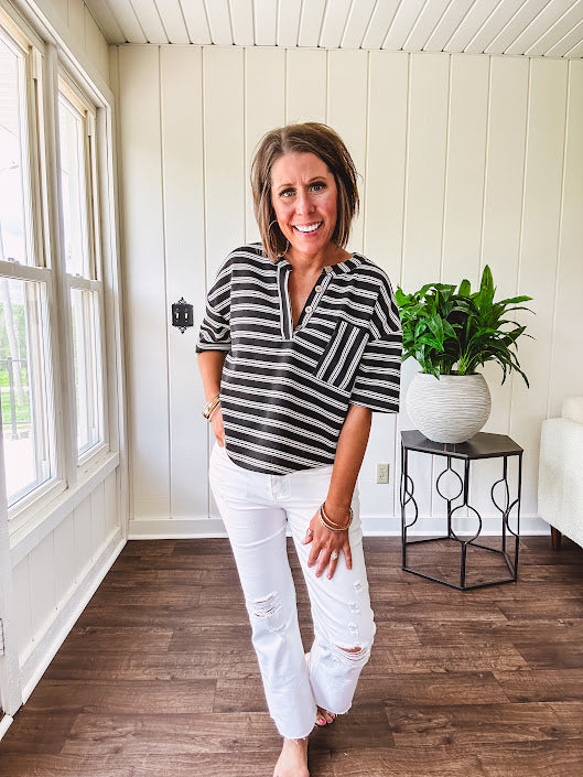 Black and white striped boxy cut Henley style knit top with 4 wooden buttons at the V neck, front pocket, short sleeves and shorter U shaped hem.