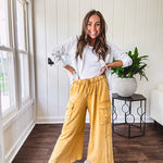 Washed mustard colored wide leg terry knit pants with a raw hem and elastic drawstring waist and oversized pockets.