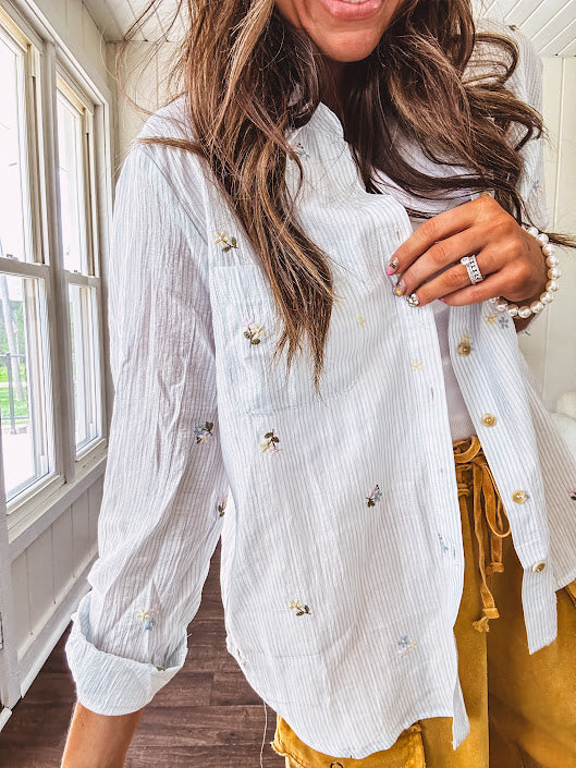 Thin, lightweight long sleeved button down blouse featuring white and blue or olive stripes adorned with small pastel floral embroidery throughout.