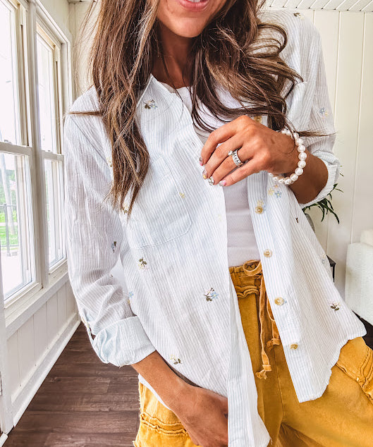 Thin, lightweight long sleeved button down blouse featuring white and blue or olive stripes adorned with small pastel floral embroidery throughout.