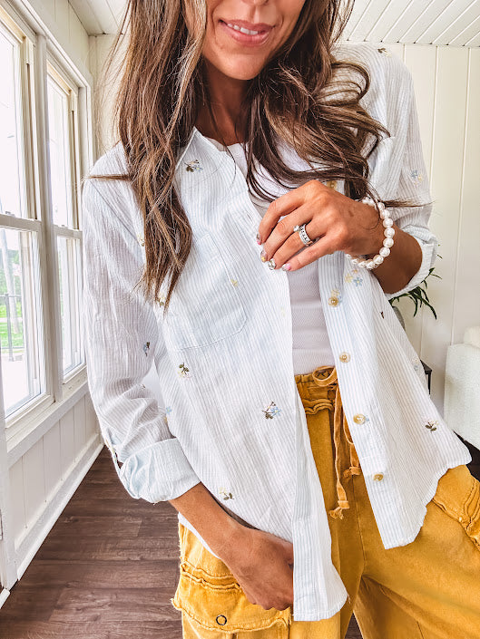 Thin, lightweight long sleeved button down blouse featuring white and blue or olive stripes adorned with small pastel floral embroidery throughout.