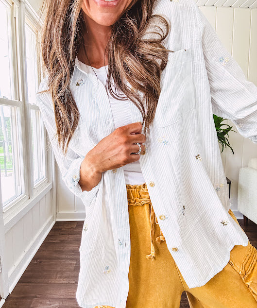 Thin, lightweight long sleeved button down blouse featuring white and blue or olive stripes adorned with small pastel floral embroidery throughout.