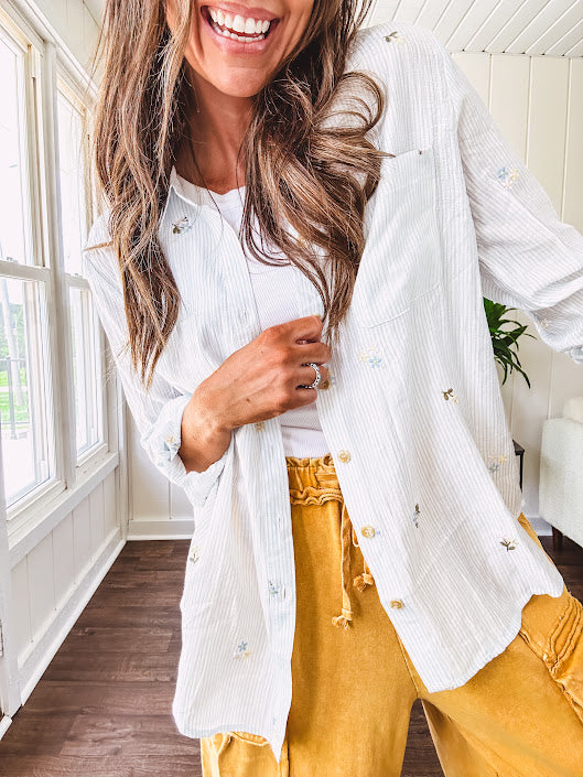 Thin, lightweight long sleeved button down blouse featuring white and blue or olive stripes adorned with small pastel floral embroidery throughout.
