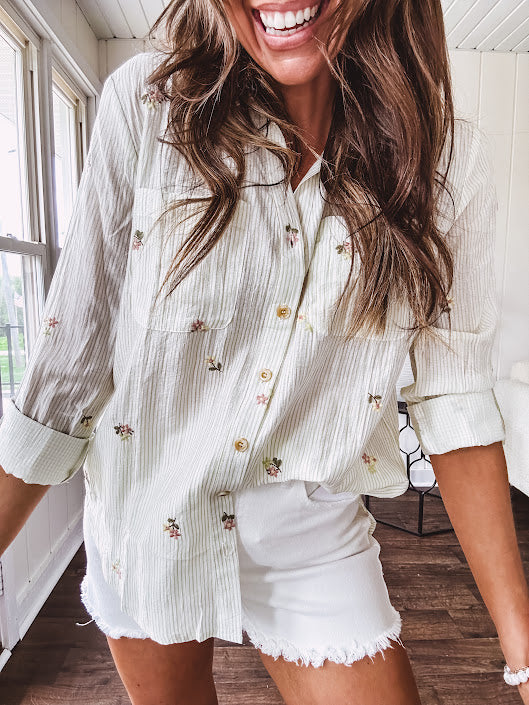 Thin, lightweight long sleeved button down blouse featuring white and blue or olive stripes adorned with small pastel floral embroidery throughout.