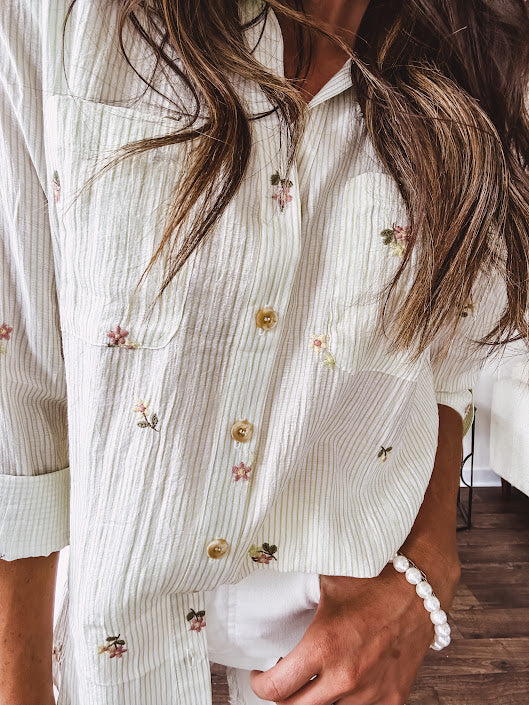 Thin, lightweight long sleeved button down blouse featuring white and blue or olive stripes adorned with small pastel floral embroidery throughout.