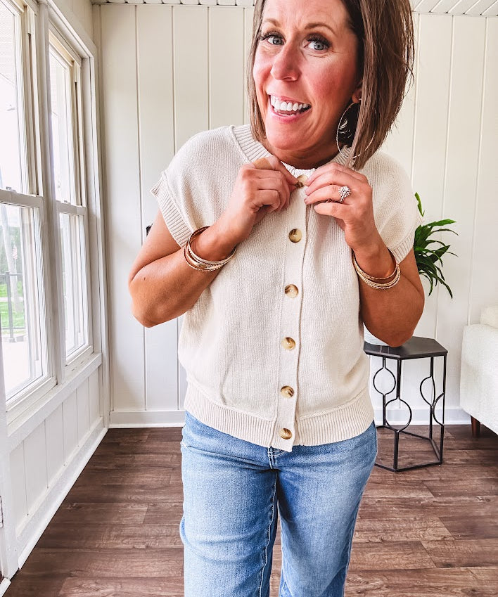 Soft, woven sweater vest with cap sleeves and faux wooden buttons down the front available in cream, sage and blush.