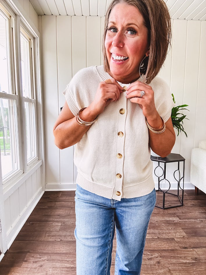 Soft, woven sweater vest with cap sleeves and faux wooden buttons down the front available in cream, sage and blush.
