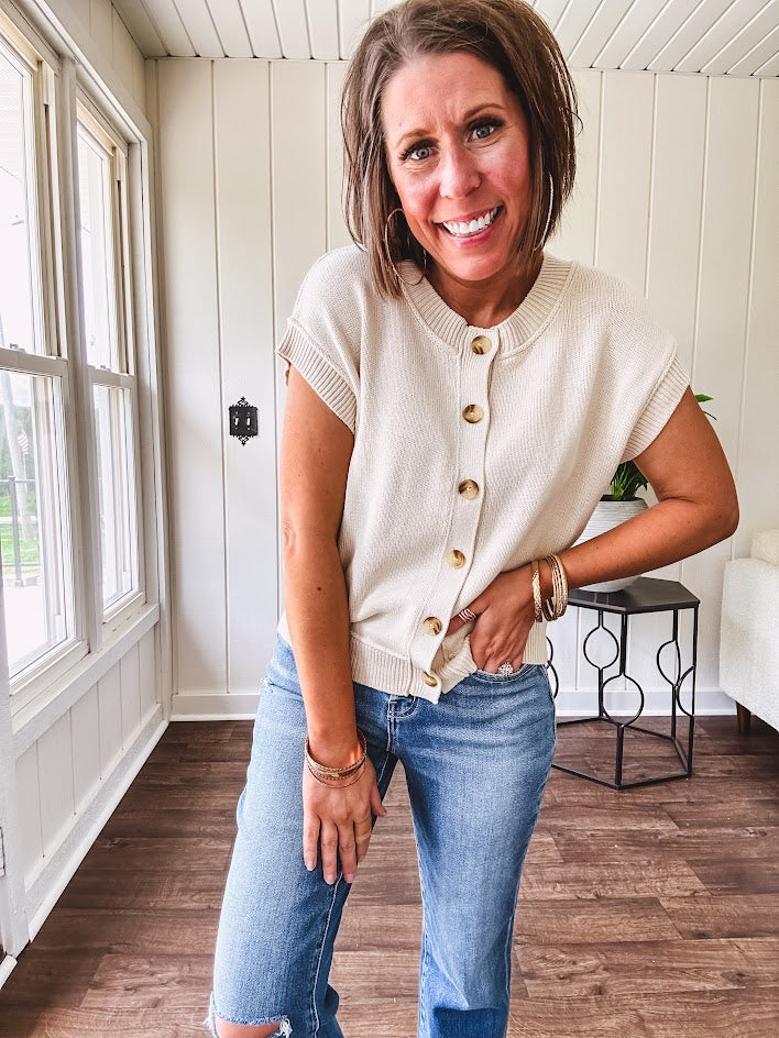Soft, woven sweater vest with cap sleeves and faux wooden buttons down the front available in cream, sage and blush.