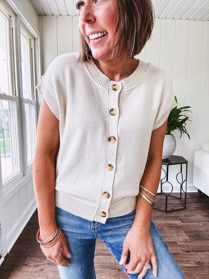 Soft, woven sweater vest with cap sleeves and faux wooden buttons down the front available in cream, sage and blush.